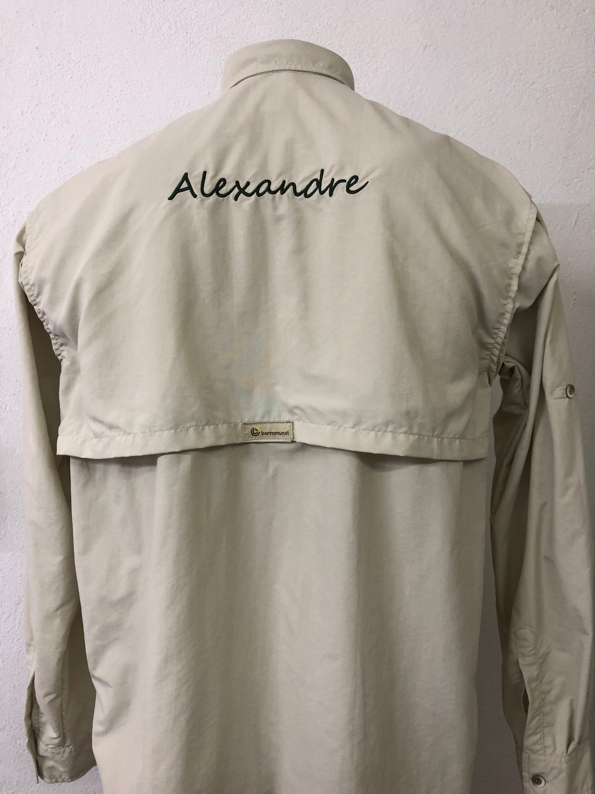 Costas de uma camisa bege com o nome Alexandre bordado em verde